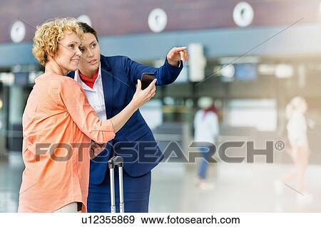 Portrait of mature woman showing her smartphone while airport staff pointing direction View Large Photo Image Stock Photo - Portrait of mature woman showing her smartphone while airport staff pointing direction . Fotosearch