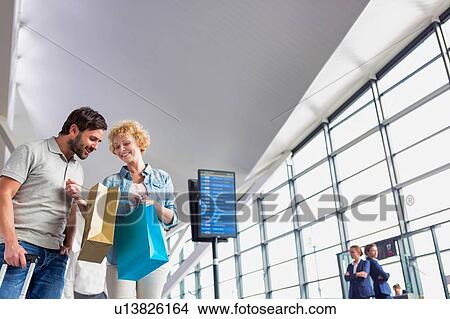 Portrait of mature woman showing present she bought in duty free with her husband at airport View Large Photo Image Picture - Portrait of mature woman showing present she bought in duty free with her husband at airport. Fotosearch