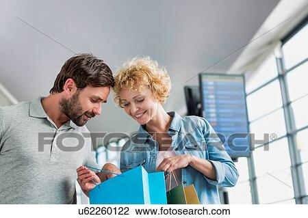 Stock Image - Portrait of mature woman showing present she bought in duty free with her husband at airport. Fotosearch
