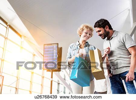 Stock Photo - Portrait of mature woman showing present she bought in duty free with her husband at airport. Fotosearch