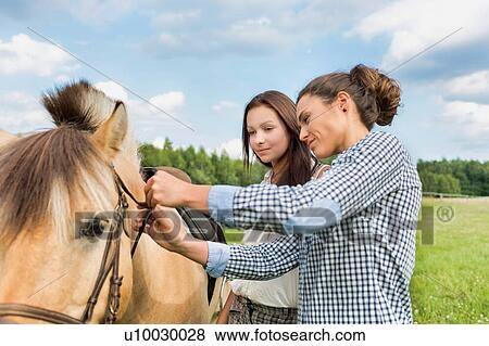 Portrait of mature woman teaching young woman on how to pull horse bit View Large Photo Image Stock Photo - Portrait of mature woman teaching young woman on how to pull horse bit. Fotosearch
