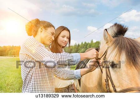 Portrait of mature woman teaching young woman on how to pull horse bit View Large Photo Image Stock Photo - Portrait of mature woman teaching young woman on how to pull horse bit. Fotosearch