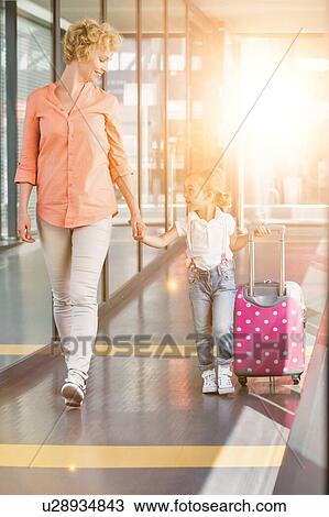 Stock Image - Portrait of mature woman walking with her daughter in arrival area at airport with lens flare . Fotosearch