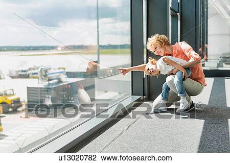 Stock Image - Portrait of mature woman with her cute little daughter looking through the window in airport. Fotosearch