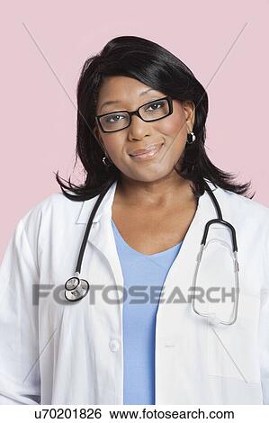 Stock Photograph - Portrait of mixed race female surgeon smiling over pink background. Fotosearch