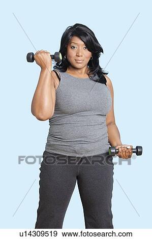 Stock Photo - Portrait of mixed race woman lifting weights over blue background. Fotosearch