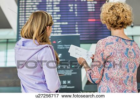 Stock Photo - Portrait of mother and daughter looking at flights on monitor in airport. Fotosearch
