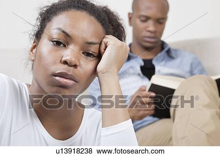 Stock Photo - Portrait of sad young woman with man reading book in background. Fotosearch