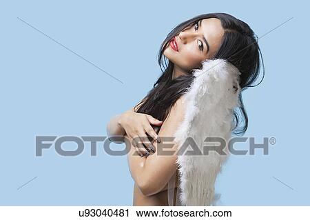 Stock Image - Portrait of seductive young woman wearing artificial wings over blue background. Fotosearch