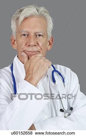 Portrait of senior male doctor with hand on chin over gray background View Large Photo Image Stock Photo - Portrait of senior male doctor with hand on chin over gray background. Fotosearch