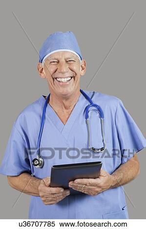 Portrait of senior male surgeon holding tablet PC over gray background View Large Photo Image Stock Photography - Portrait of senior male surgeon holding tablet PC over gray background. Fotosearch