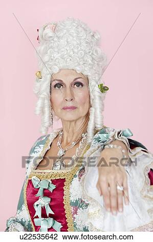 Stock Image - Portrait of senior queen stretching out her hand over pink background. Fotosearch