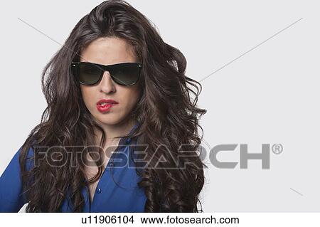 Portrait of sensuous young woman wearing sunglasses while biting lip over gray background View Large Photo Image Picture - Portrait of sensuous young woman wearing sunglasses while biting lip over gray background. Fotosearch