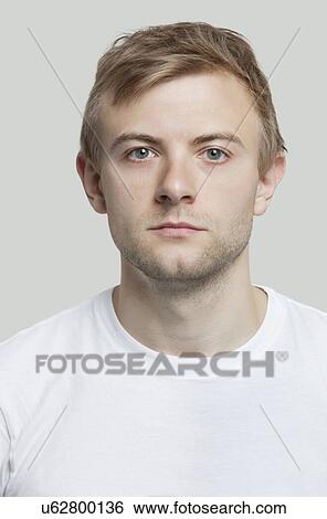 Stock Photograph - Portrait of serious young man in t-shirt against gray background. Fotosearch