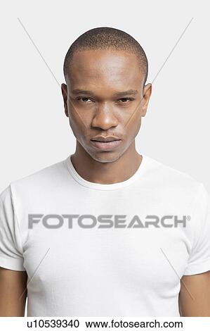 Stock Image - Portrait of serious young man in white t-shirt against white background. Fotosearch