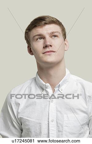 Stock Image - Portrait of serious young man looking up against gray background. Fotosearch