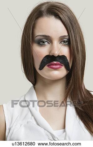 Stock Image - Portrait of serious young woman with fake mustache over gray background. Fotosearch