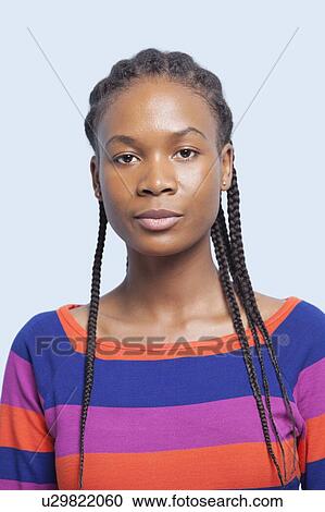Stock Image - Portrait of serious young woman with braided hair against light blue background. Fotosearch
