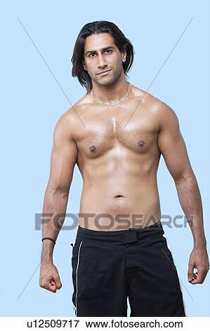 Stock Photo - Portrait of shirtless young muscular man standing over blue background. Fotosearch