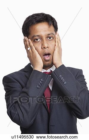 Stock Image - Portrait of shocked young businessman against white background. Fotosearch