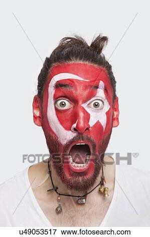 Stock Photo - Portrait of shocked young man with Turkish flag painted on face screaming against white background. Fotosearch