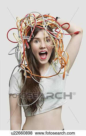 Stock Photo - Portrait of shocked young woman's head tangled with colorful cables over gray background. Fotosearch