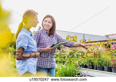 Stock Photo - Portrait of shop owner showing flowers to woman buyer . Fotosearch