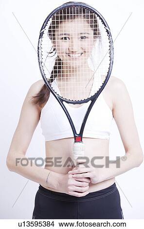 Portrait of smiling Asian woman holding tennis racket in front of her face against white background View Large Photo Image Picture - Portrait of smiling Asian woman holding tennis racket in front of her face against white background. Fotosearch