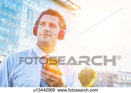 Portrait of smiling mature businessman listening to music on his smartphone with headphones on View Large Photo Image Stock Photo - Portrait of smiling mature businessman listening to music on his smartphone with headphones on . Fotosearch