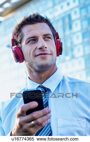 Stock Photography - Portrait of smiling mature businessman listening to music on his smartphone with headphones on . Fotosearch