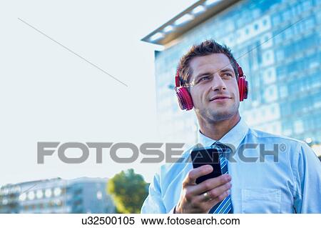 Stock Photography - Portrait of smiling mature businessman listening to music on his smartphone with headphones on . Fotosearch