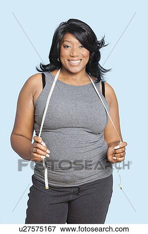 Stock Photo - Portrait of smiling mixed race woman with measuring tape over blue background. Fotosearch