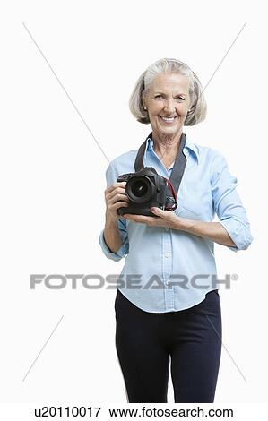 Stock Photo - Portrait of smiling senior female photographer with camera against white background. Fotosearch