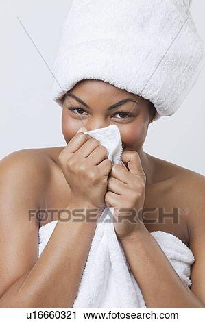 Stock Image - Portrait of smiling young African American woman wrapped in towel over white background. Fotosearch