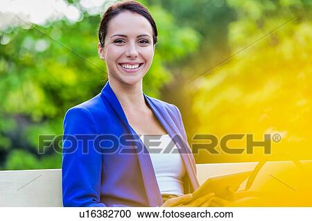 Stock Image - Portrait of Smiling young attractive businesswoman holding digital tablet while standing in park. Fotosearch