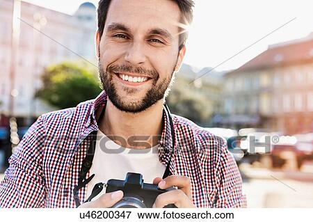Portrait of Smiling Young attractive man holding camera with lens flare in background View Large Photo Image Stock Photo - Portrait of Smiling Young attractive man holding camera with lens flare in background. Fotosearch
