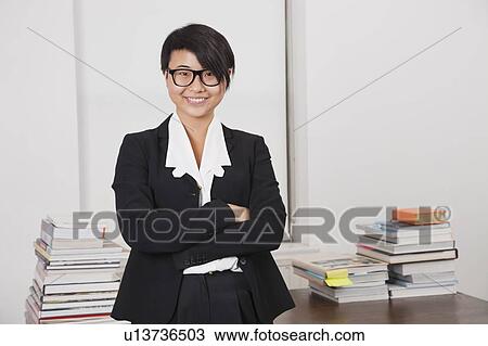 Portrait of smiling young businesswoman with stack of books on desk in office View Large Photo Image Stock Image - Portrait of smiling young businesswoman with stack of books on desk in office. Fotosearch