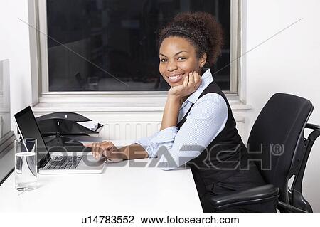 Portrait of smiling young businesswoman using laptop at desk in office View Large Photo Image Stock Image - Portrait of smiling young businesswoman using laptop at desk in office. Fotosearch
