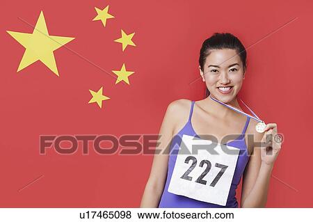 Stock Photo - Portrait of smiling young female medalist standing against Chinese flag. Fotosearch
