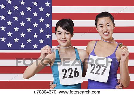 Stock Image - Portrait of smiling young medalists standing against American flag. Fotosearch