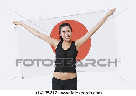 Stock Image - Portrait of smiling young woman holding Japanese flag over white background. Fotosearch