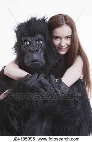 Stock Photography - Portrait of smiling young woman hugging man in gorilla costume against white background. Fotosearch