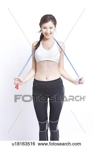 Portrait of smiling young woman exercising with skipping rope against white background View Large Photo Image Stock Photograph - Portrait of smiling young woman exercising with skipping rope against white background. Fotosearch