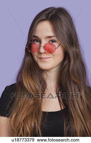 Stock Photo - Portrait of smiling young woman wearing sunglasses over purple background. Fotosearch