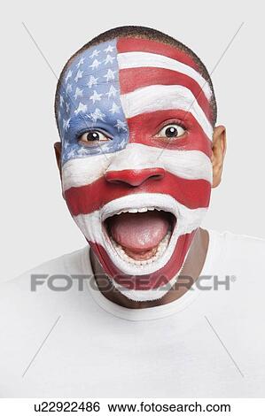 Stock Photograph - Portrait of surprised young man with North American flag painted on face shouting against white background. Fotosearch
