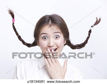 Stock Image - Portrait of surprised young woman with braids curling upwards against white background. Fotosearch