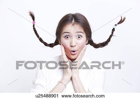 Stock Image - Portrait of surprised young woman with braids curling upwards against white background. Fotosearch