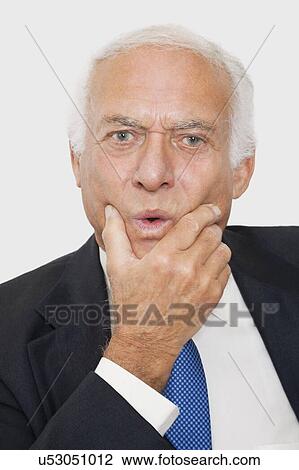 Stock Image - Portrait of suspicious elderly businessman against white background. Fotosearch