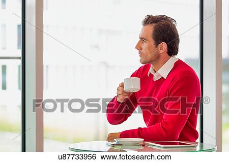 Stock Photograph - Portrait of thougtful businessman sitting while drinking coffee in lobby. Fotosearch