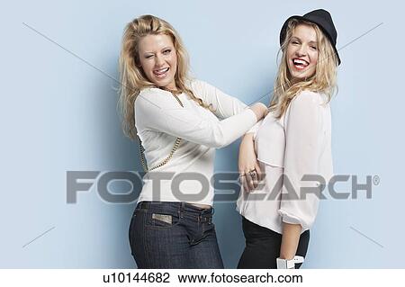 Portrait of two playful young women sticking out tongues against light blue background View Large Photo Image Stock Image - Portrait of two playful young women sticking out tongues against light blue background. Fotosearch